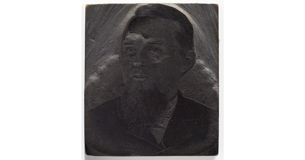 A metal printing block with a portrait of the head and shoulders of a man with a goatee wearing a suit.