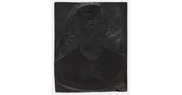 A metal printing block with a portrait of the head and shoulders of a man with a walrus-style mustache, wearing a suit.
