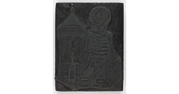 An engraved wood printing block depicting a skeleton standing in front of a table with a bottle and two glasses.