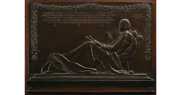 A bronze relief of a man reclining on a chaise with a tablet and pen in hand.