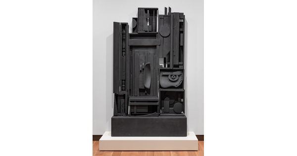 A black-painted wood sculpture with many compartments that include fragments of things such as a bedpost, juggling pin, and a chair.