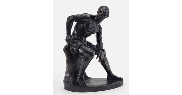 A bronze sculpture of a muscled Black man with manacles on his wrists leaning forward as he sits on a tree stump.