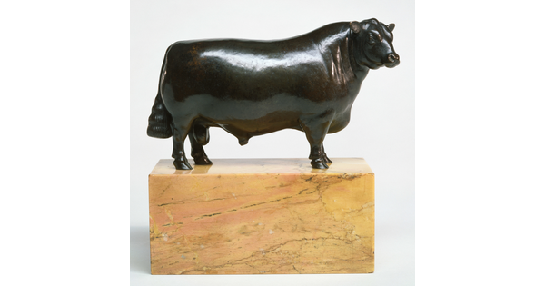 A bronze sculpture of a bull with a thick body and chest standing on a stone base.