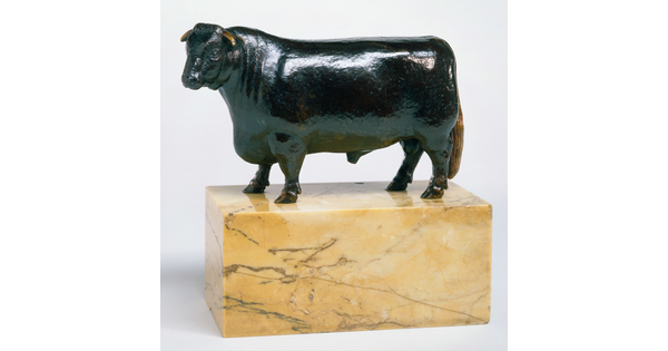 A bronze sculpture of a bull with a thick body and chest standing on a stone base.