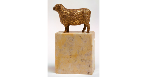 A bronze sculpture with a gold finish of a wooly sheep standing on a stone base.