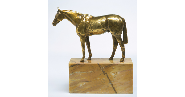 A yellow bronze sculpture of a muscular horse with a long tail on a base of yellow marble. 