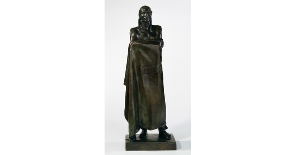 A bronze sculpture of a Native American man who stands wrapped in a blanket.