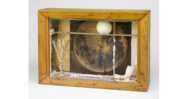 A wood shadowbox containing a pipe, a white ball with gray speckles, a picture of the moon, and a glass goblet.