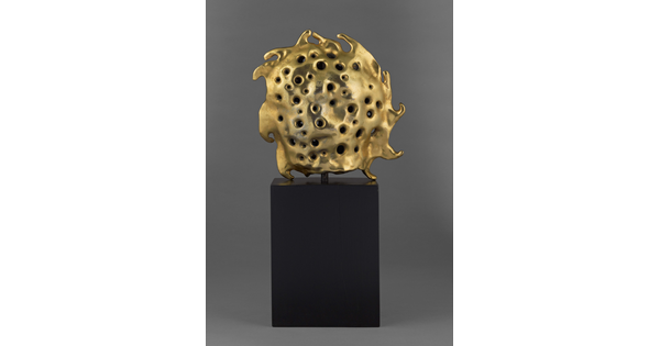 A bronze sculpture of a gold sun sitting atop a tall, dark rectangular base.