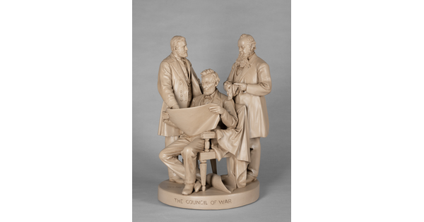 A sculpture of Abraham Lincoln, seated, reading a paper between two standing men.