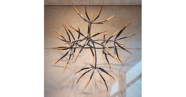 A large, hanging sculpture of seven clusters of seven elongated, tapered forms that resemble flower petals and stems.