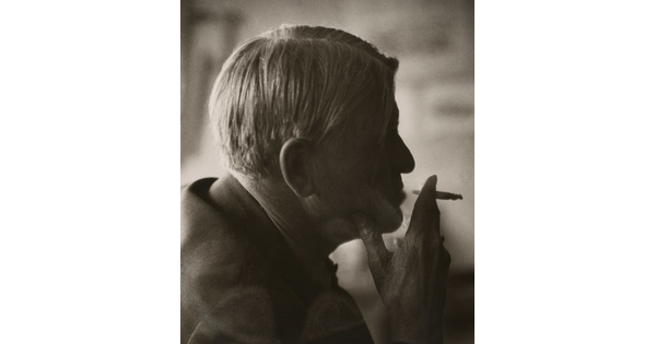 A sepia-toned photograph of a man's head in profile holding a cigarette posed in front of his lips.