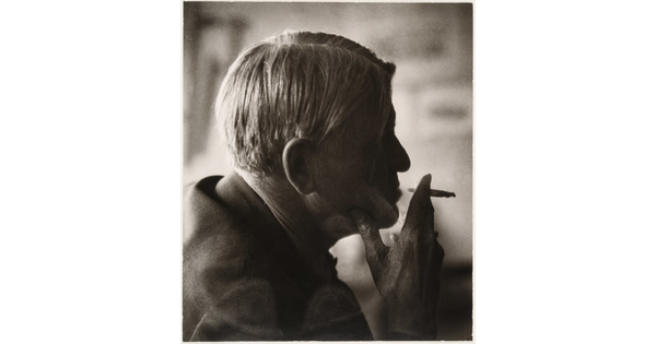 A sepia-toned photograph of a man's head in profile holding a cigarette posed in front of his lips.