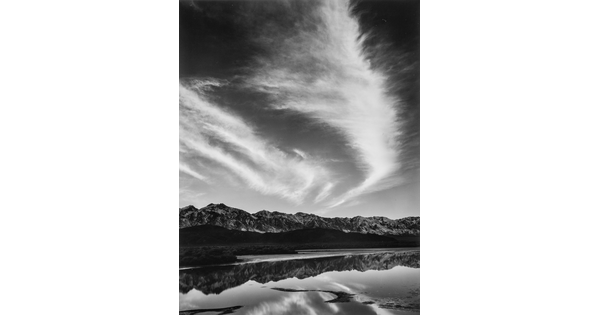 A black-and-white landscape photograph of mountains and clouds that reflect on the still water in the foreground.