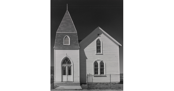 A black-and-white photograph of a two-story church with white clapboard siding and arched windows and doors.