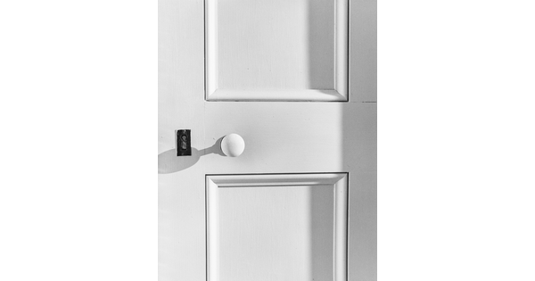 A black-and-white close-up photograph of a white, paneled door, with a metal keyhole on the left side and a white doorknob to the right of it.