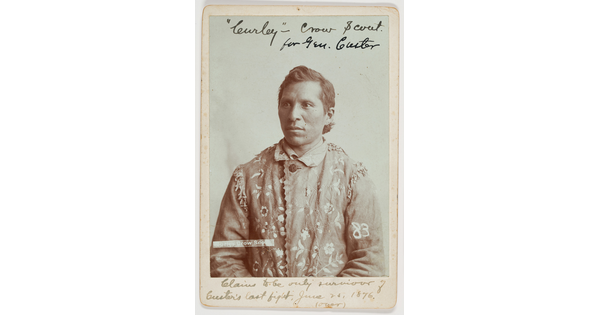 A sepia-toned portrait of an Indigenous man wearing a hide jacket with decorative stitching.