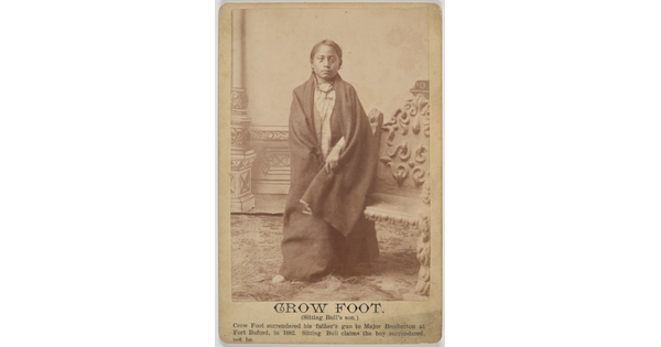 A sepia-toned portrait photograph of an Indigenous boy wrapped in a blanket.