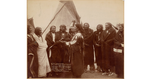 A sepia-toned photograph of Indigenous men wrapped in blankets meeting in front of a tipi.