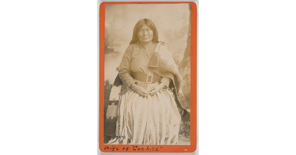 A sepia-toned formal portrait photograph of an Indigenous woman wearing a dress with a belt, and a blanket draped on her shoulders.