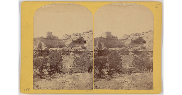 Two almost identical side-by-side sepia-toned photographs of cave dwellings in a high cliff with scrubby vegetation in the foreground.