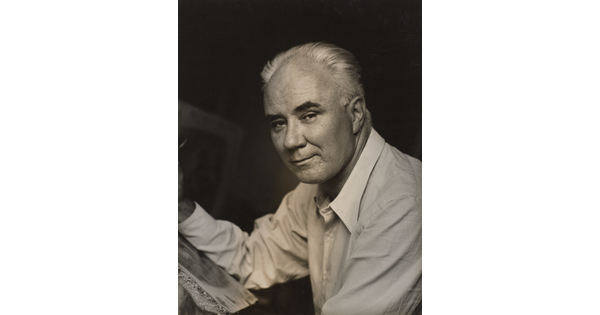 A black-and-white photograph of a middle-aged White man in three-quarter view leaning on something in front of him with his forearm.