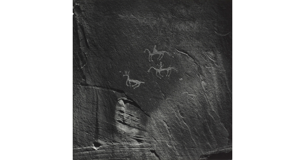 A black-and-white photograph of rock paintings depicting people on horseback and a deer.