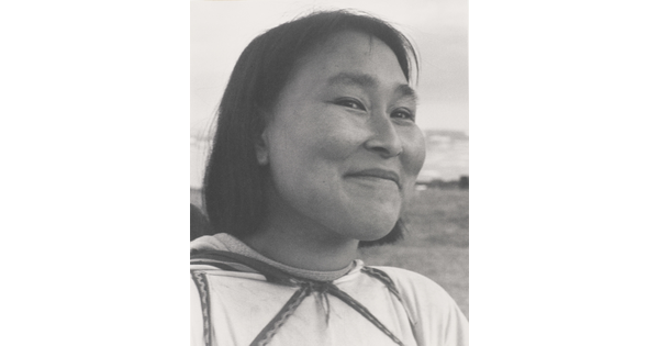 A black-and-white photograph of a close-up of a smiling Indigenous woman with short dark hair wearing a light-colored shirt.
