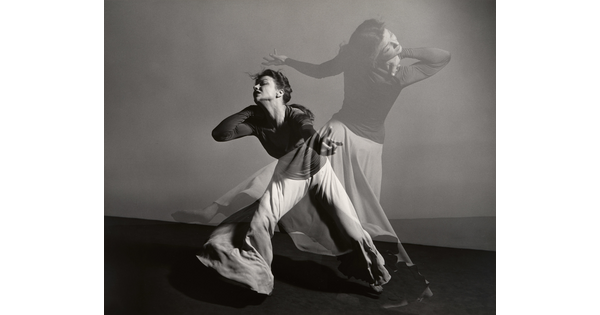 A double-exposed, black-and-white photograph of a female figure dancing dramatically.