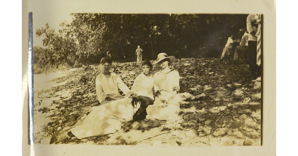 A sepia-toned photograph of four White women, three sitting and one lying with her head on the lap of another, on a rocky slope.