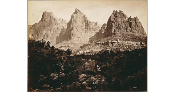 A black-and-white photograph of three large, majestic crags with rocks and vegetation in the foreground.