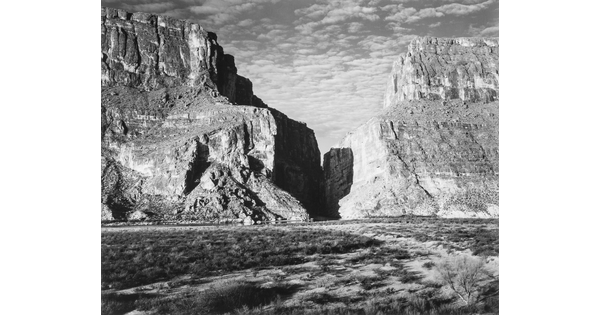 A black-and-white photograph of a canyon between two large mountains.