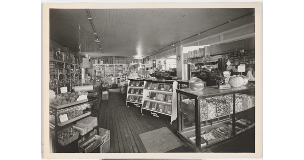 A black-and-white photograph of the interior of a grocery store from the early 20th century.
