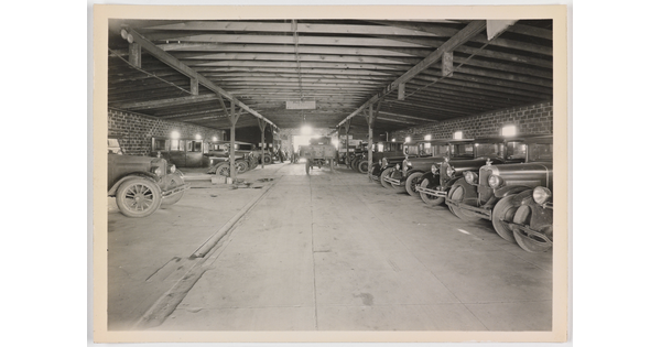 A black-and-white photograph of early models of cars in a covered garage.
