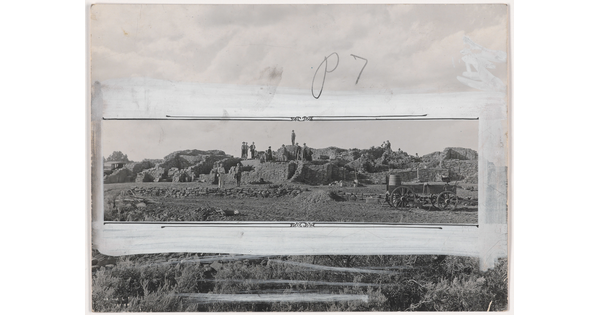 A black-and-white photograph of people standing on an excavation site; crop marks and white paint mark how the photo should be cropped.