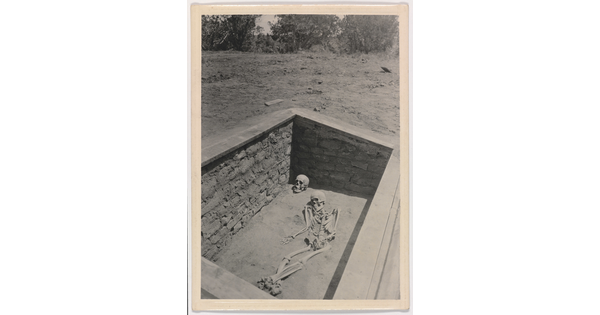 A black-and-white photograph of an archaeological grave site with a full human skeleton laying beside a skull.