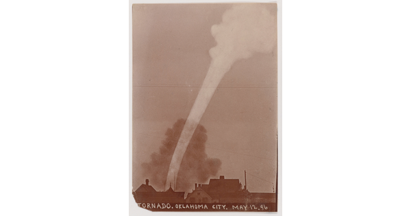 A sepia-toned photograph of a white funnel cloud above the silhouette of a town.