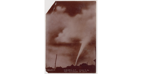 A sepia-toned photograph of a white funnel cloud above the silhouette of a town.
