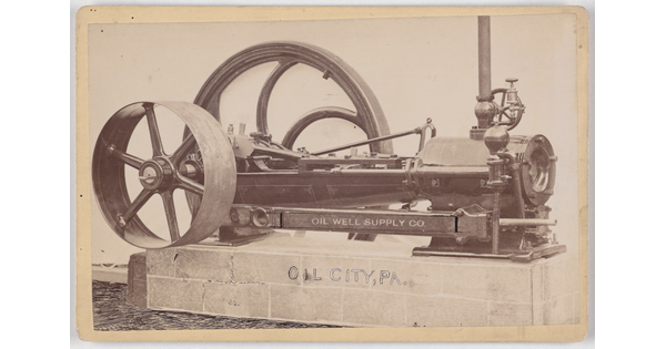 A black-and-white photograph of a machine with two wheels of varying sizes sitting on a concrete base.