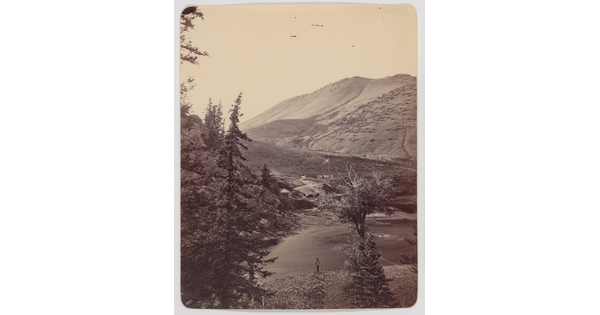 A black-and-white photograph of an aerial view of a mountain lake and a person fishing on the shore.