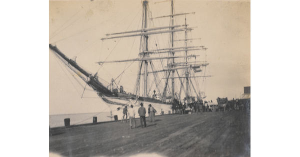 A black-and-white photograph of people on a dock looking at a large ship.