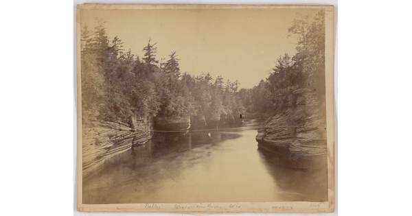 A black-and-white photograph of a wide calm river lined with trees and rock formations.