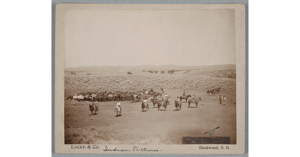 A black-and-white photograph of a large group of cowboys on horseback lined up in an open field.