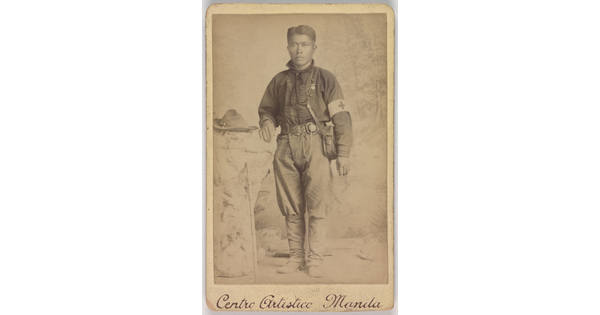 A black-and-white photograph of a medium-skinned soldier with a canteen slung across his chest and wearing a Red Cross armband.