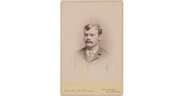 A black-and-white portrait photograph of a White man with a mustache wearing a jacket and tie.