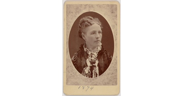 A black-and-white oval-shaped portrait photograph of a White woman, hair pulled up, wearing a dress with a high ruffled neck.