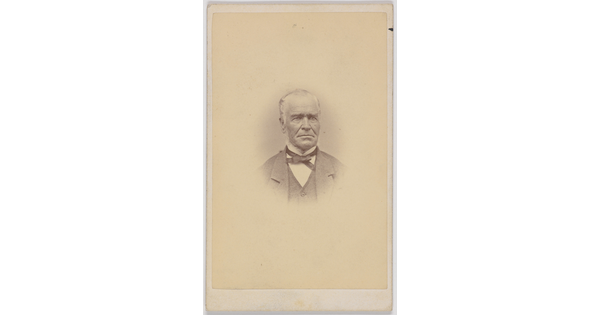 A black-and-white portrait photograph of an older White man, balding, wearing a bow tie, jacket, and vest.