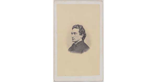 A black-and-white portrait photograph of a young White man in profile with dark wavy hair, wearing a dark overcoat.