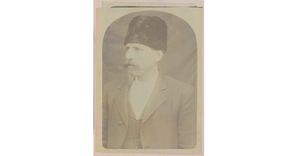 A faded sepia-toned portrait of a White man with a handlebar moustache wearing a fur Cossack-stye hat and a three-piece suit.
