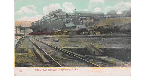 A color postcard of railroad tracks beside an industrial building.